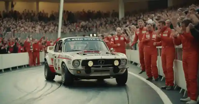 A scene depicting race car drivers on an indoor track, surrounded by excited spectators.