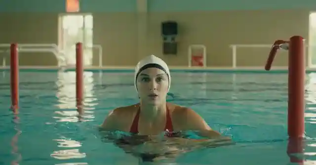 Swimmer exercising in an aquatic center pool featuring water poles and a lifeguard.
