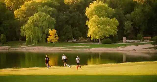 Friends playing soccer next to the serene lake surrounded by lush greenery at Lakeview Park in Peoria.