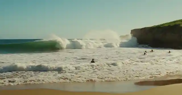 A beach scene featuring people swimming in the surf with waves crashing nearby.