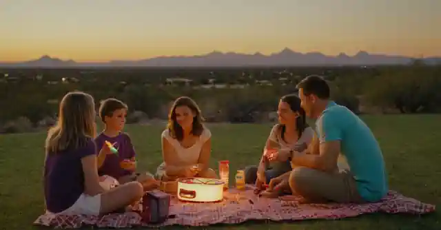 A family enjoying an outdoor evening activity in Phoenix; parents setting up a picnic while kids play with frisbees or glow sticks.