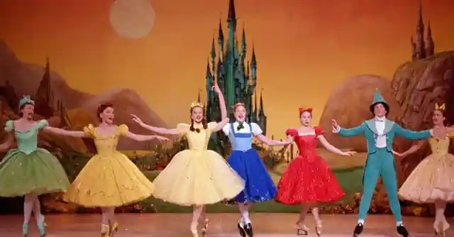 Ice skaters performing choreographed routines inspired by the animated film series from The Wizard of Oz, with elaborate costumes and sets against a backdrop depicting different fantastical realms.
