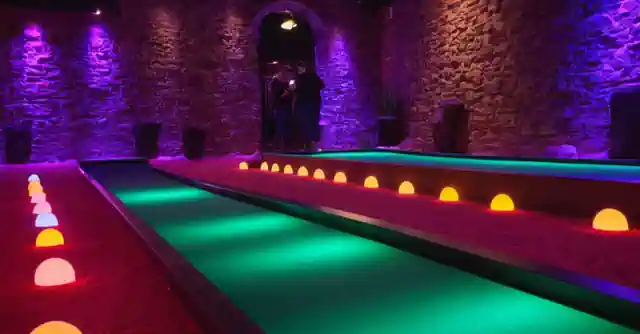 A person putting under colorful lights and obstacles at the Glow Putt Mini Golf course.