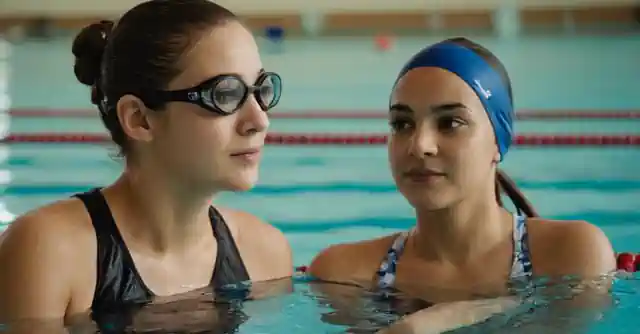 Person observing performance metrics on the dashboard while swimming with a coach.