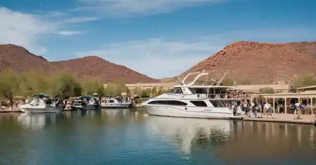 The image shows various water vessels docking and undocking at Lake Pleasant in Pebble Springs, AZ. Its a part of the activities offered by Paqua Park, where one can observe boats with families on board enjo**, engage in fishing or other water-based leisure activities).