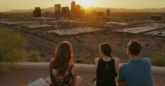 A sunset view over Phoenix landscape from the roo**m featuring people and the downtown high rise buildings.