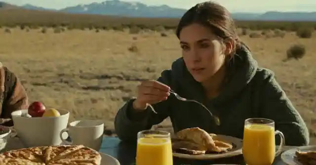 Persona desayunando frente a un belén navideño mientras nevada en el fondo.
