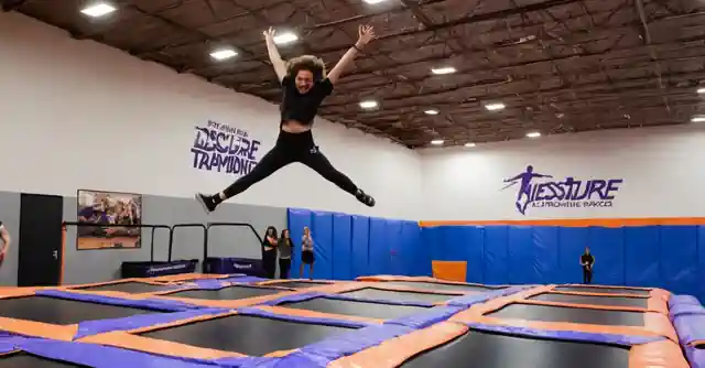 A person jumping enthusiastically on a trampoline at Altitude Trampoline Park in Phoenix, with the signboard reading Descubre la emoción (Experience the thrill) visible.