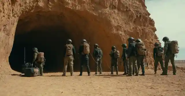 Diferentes grupos montando una cueva, con cascos y cuerdas colgadas contra un fondo desértico.