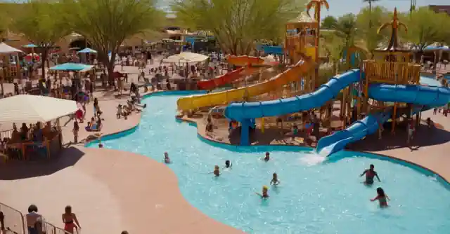 An image showcasing various water play areas and attractions for young children, including colorful slides, pools, and fountains at the Tempe Marketplace aqua park.