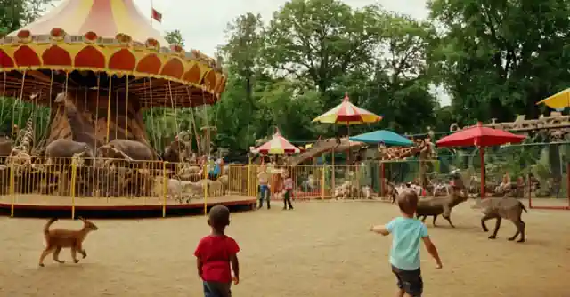 Children joyfully playing in an amusement park surrounded by various animals at a zoo.